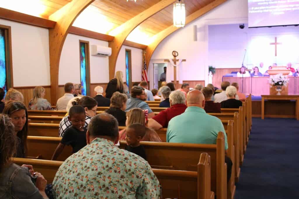 Image of the inside of the church santuary with members sitting in the pews. Viewed from the back toward the platform.